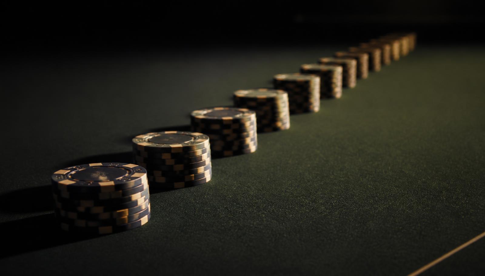 A long receding line of identical stacks of casino chips on dark green baize, fading into shadow, suggesting repeated wagers